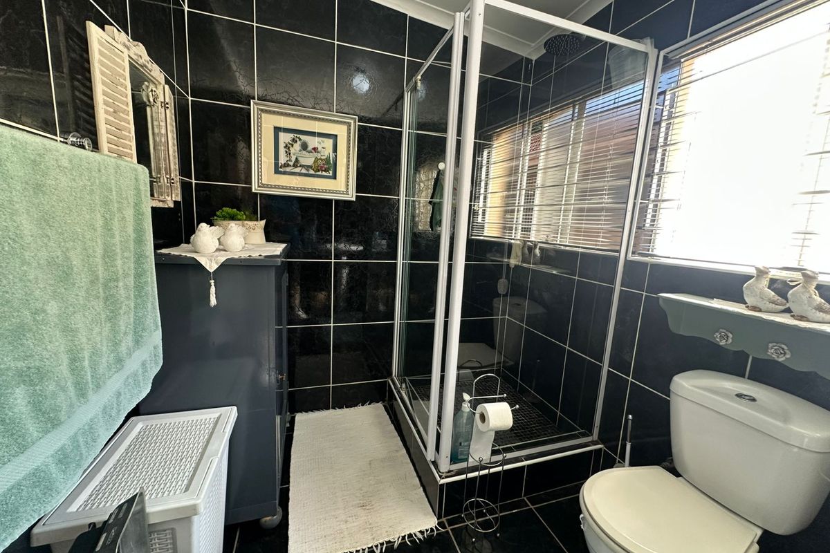 A bathroom featuring a corner shower enclosure, a white toilet, and dark high-gloss wall and floor tiles.