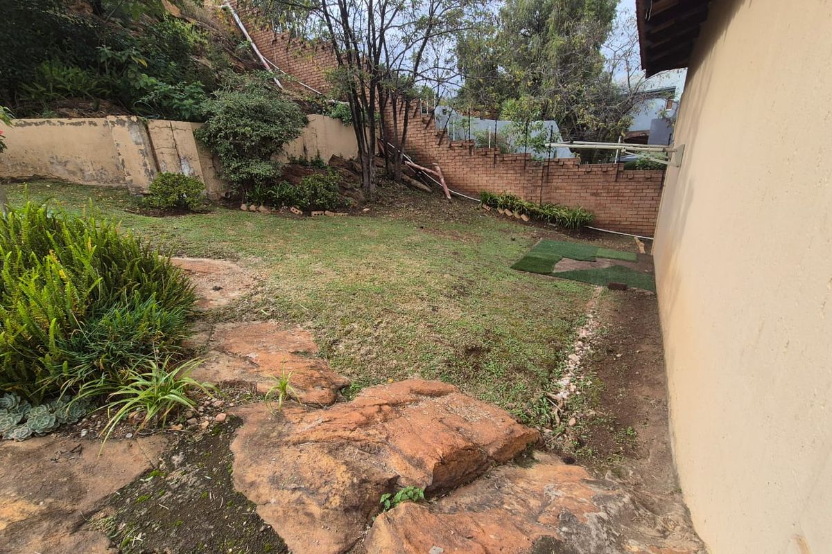 A rear garden area featuring natural rock formations, a lawn, and a brick boundary wall with visible signs of weathering.