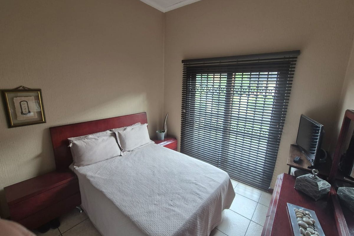 A bedroom featuring tiled flooring and a sliding glass door with fitted venetian blinds, providing natural light and access to the exterior.