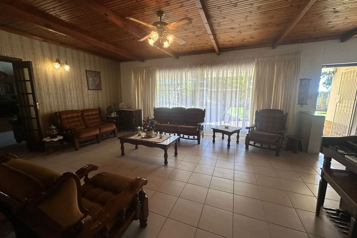 Spacious living room featuring a rustic exposed timber ceiling, ceiling fan, and neutral ceramic floor tiles with large sliding doors providing natural light.