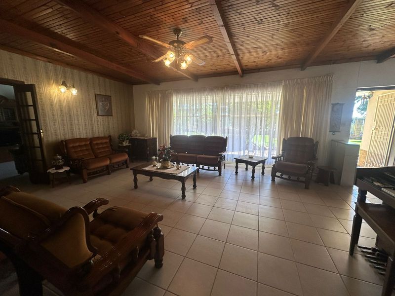 Spacious living room featuring a rustic exposed timber ceiling, ceiling fan, and neutral ceramic floor tiles with large sliding doors providing natural light.