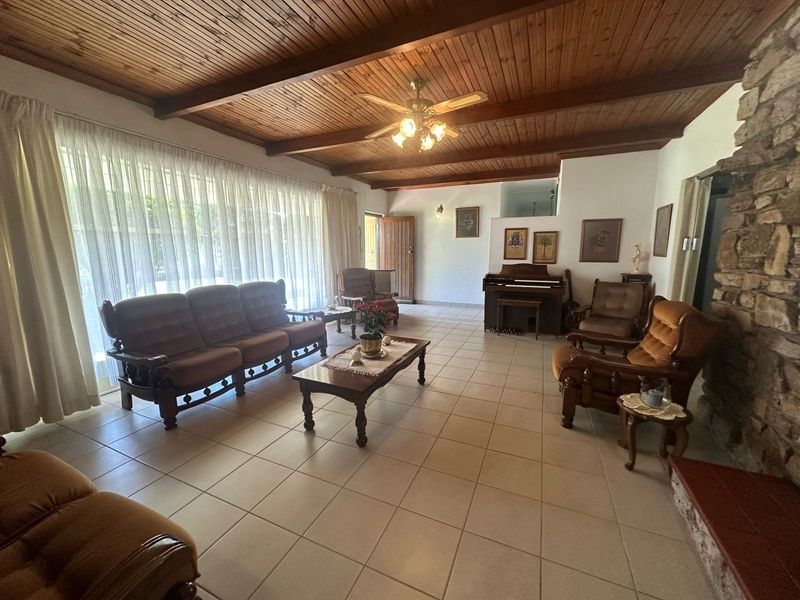 Spacious living room featuring a rustic exposed timber beam ceiling, tiled flooring, and a prominent stone fireplace, offering a warm and traditional atmosphere.