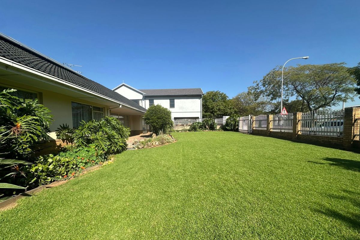 A well-maintained rear garden featuring a spacious lawn, paved patio area, and secure perimeter walling with metal fencing.