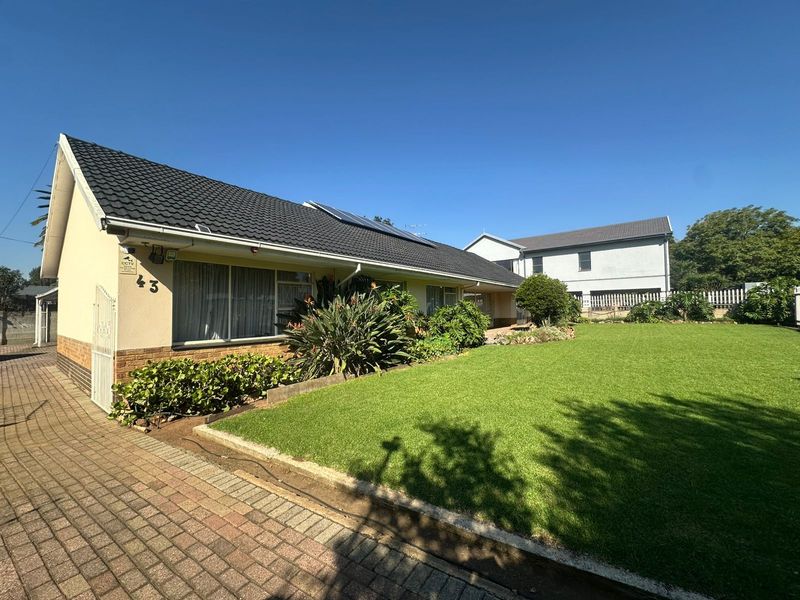 A well-maintained single-story home featuring a tiled roof, solar panels, a paved driveway, and a neatly landscaped front lawn.