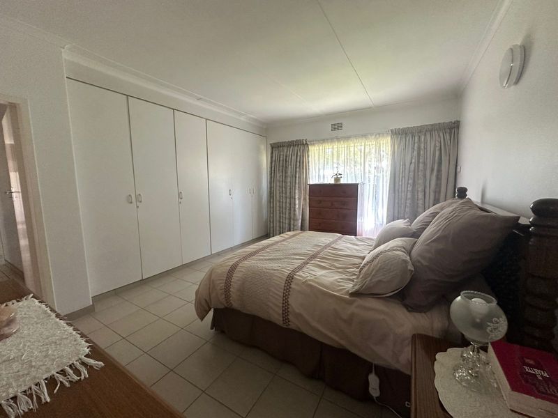 A spacious bedroom featuring extensive built-in cupboards, neutral tiled flooring, and a coved ceiling, offering a functional and well-maintained living space.