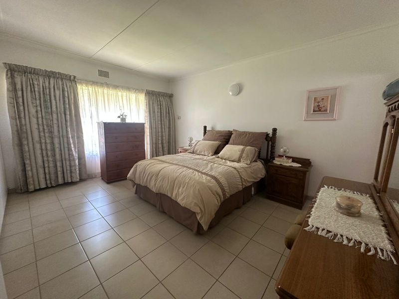 A spacious bedroom featuring neutral tiled flooring, large windows with curtain rails, and a wall-mounted light fixture.