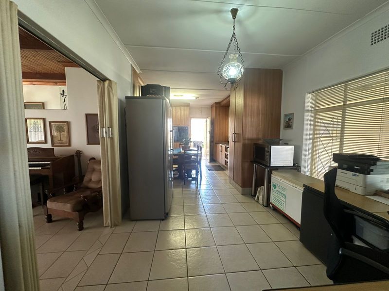 Open plan living and kitchen area featuring tiled flooring, built-in wooden cabinetry, and natural light through venetian blinds.
