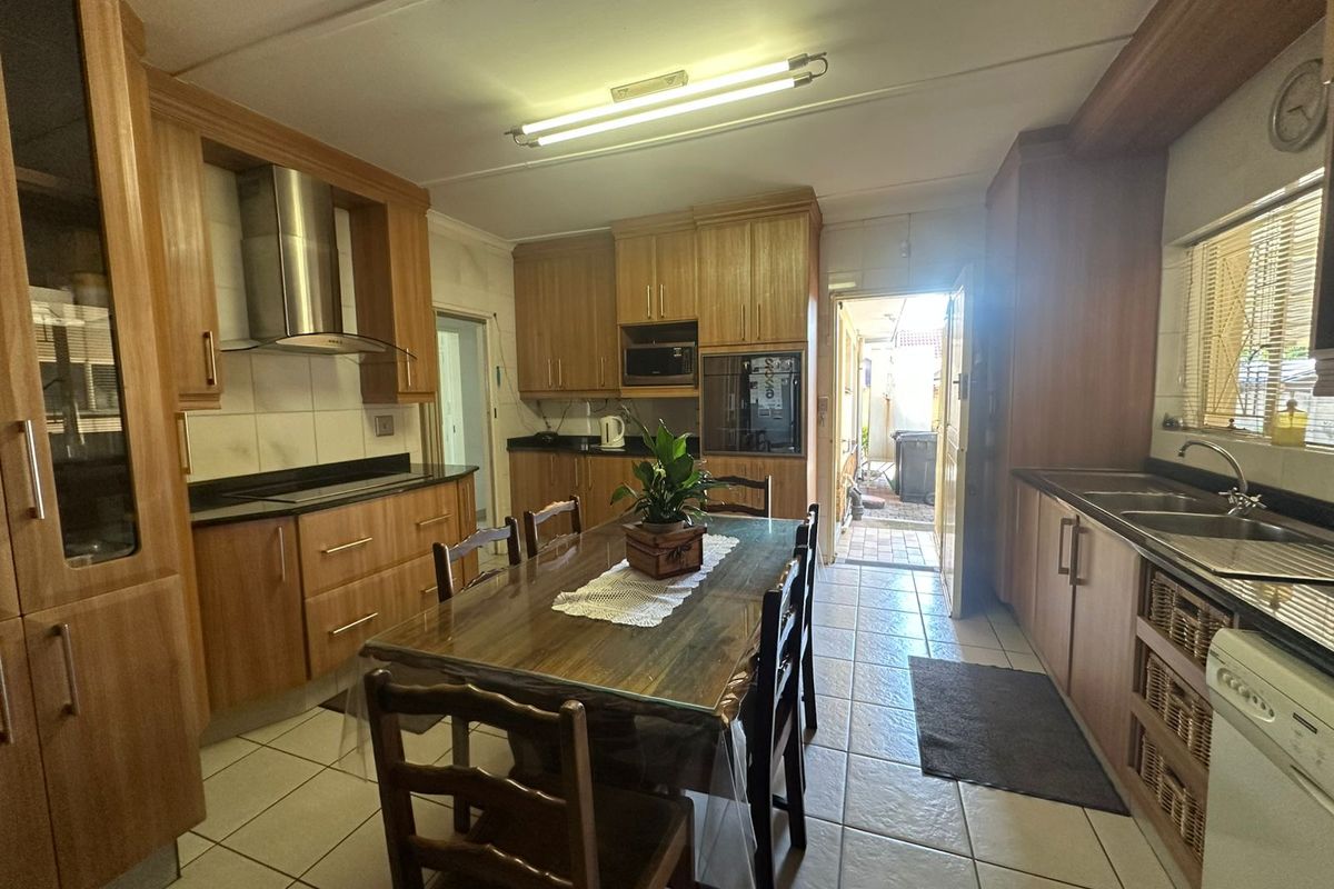 A functional kitchen featuring wooden cabinetry, granite countertops, built-in oven, and stainless steel extractor fan, with direct access to an outdoor area.