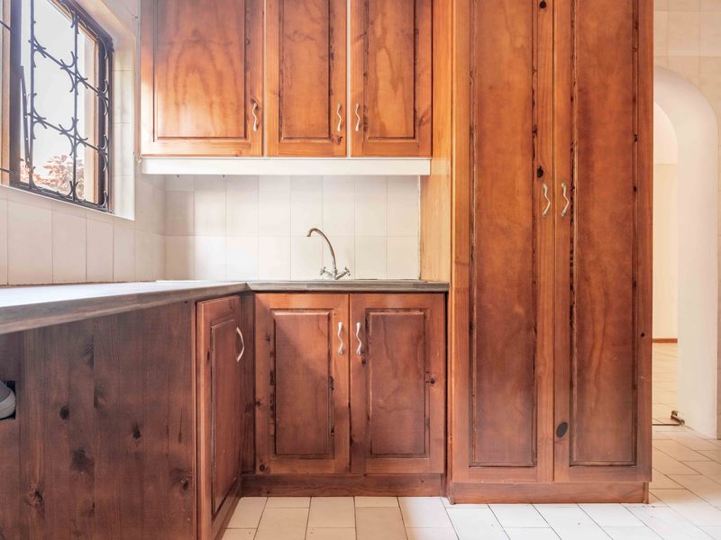 A functional scullery area featuring traditional wooden cabinetry, tiled backsplash, and tiled flooring, offering potential for a modern kitchen upgrade.