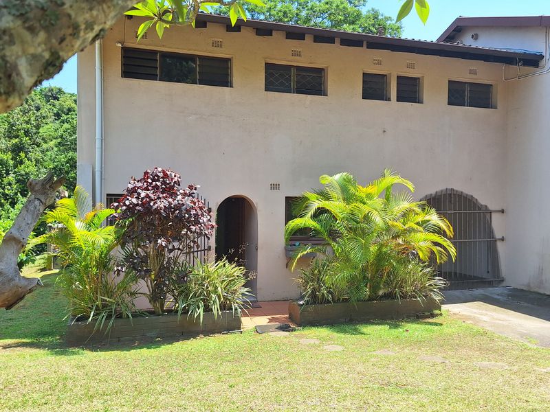 Front elevation of a townhouse featuring an arched entrance, security gate, and established garden beds with a concrete driveway.