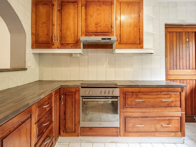 A functional kitchen featuring wooden cabinetry, a built-in oven with electric cooktop, extractor fan, and tiled backsplash, offering a classic layout ready for modernization.