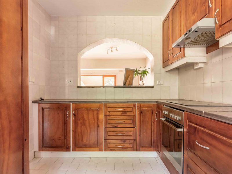 A functional kitchen featuring traditional wooden cabinetry, built-in oven, electric cooktop, and a convenient serving hatch opening into the adjacent living area.
