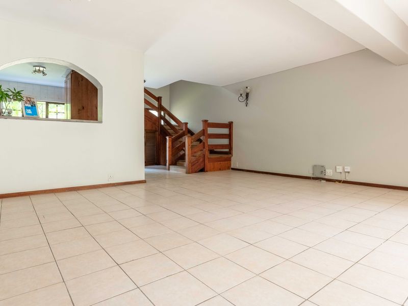 Spacious open-plan living area featuring neutral tiled flooring, a wooden staircase with a balustrade, and a decorative archway looking into the kitchen.