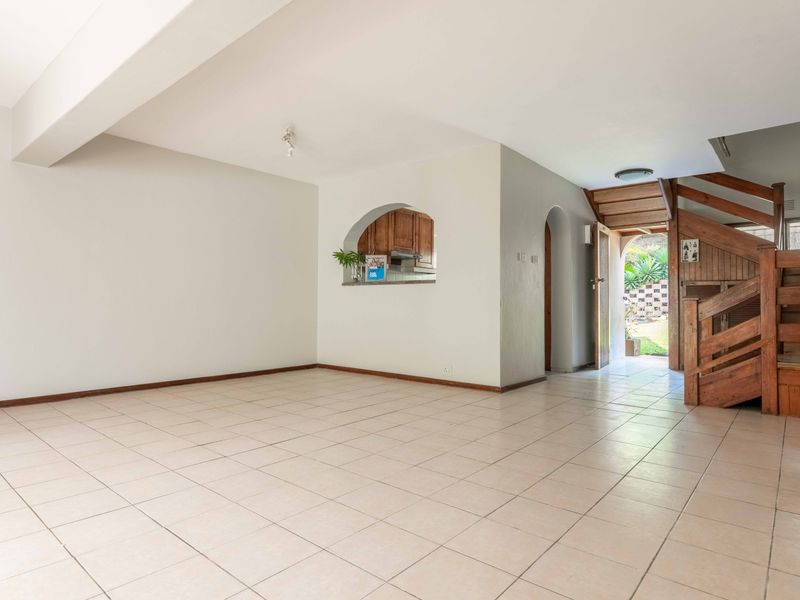 Spacious open-plan living area featuring tiled flooring, a wooden staircase, and a convenient pass-through window connecting to the kitchen area.