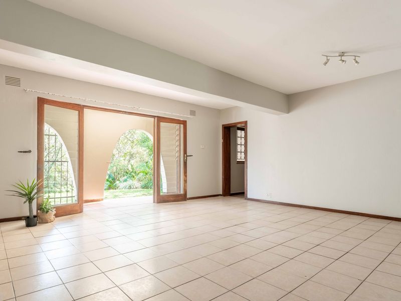 Spacious, light-filled living area featuring neutral tiled flooring and large wooden sliding doors opening onto a garden patio.