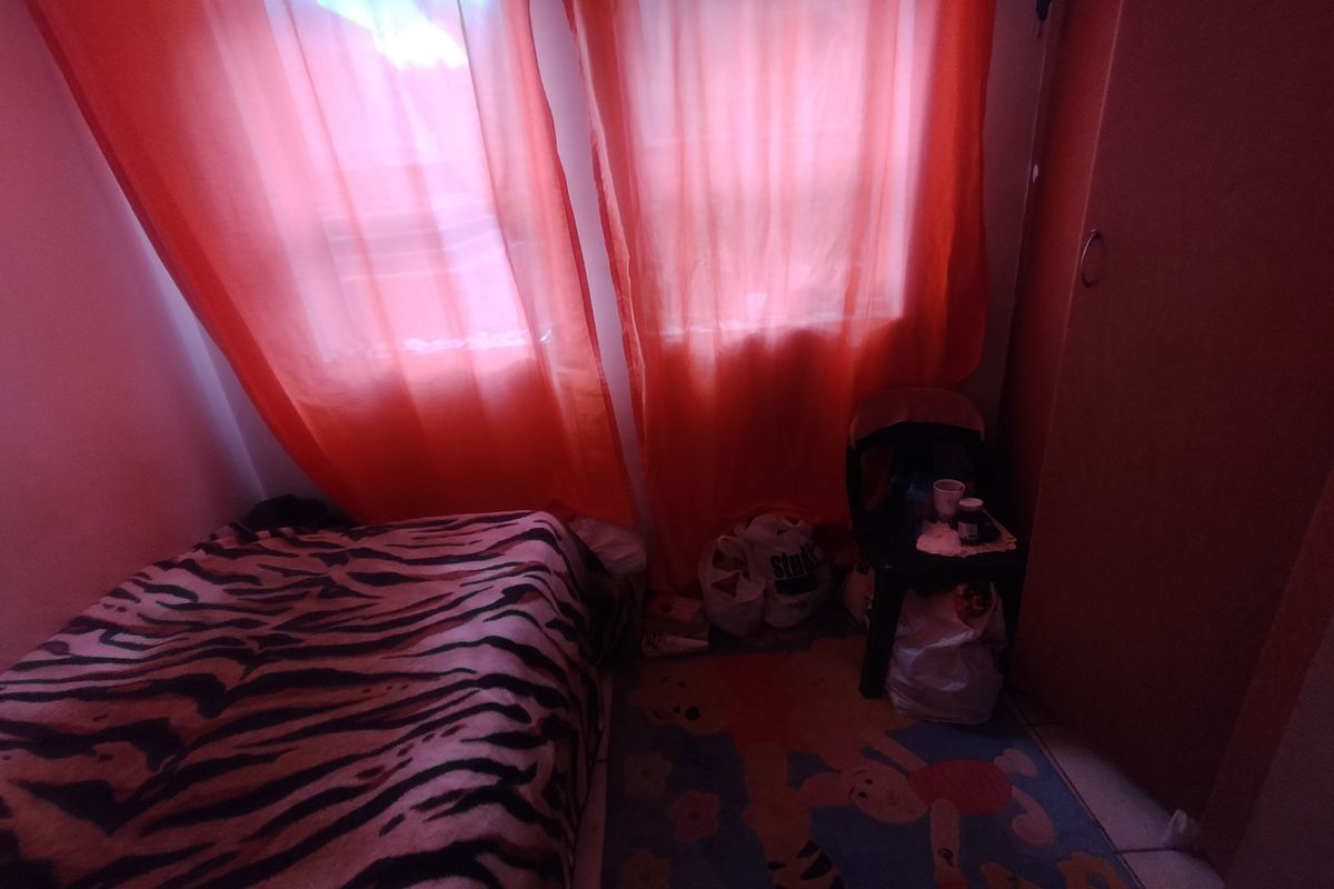 A bedroom featuring a built-in wardrobe and tiled flooring, currently illuminated by natural light through window coverings.