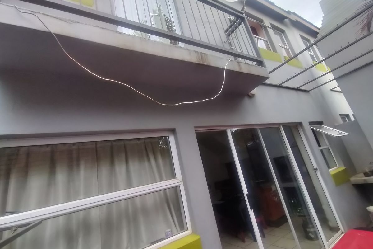 Rear exterior view of the townhouse featuring a balcony with metal railing, sliding glass doors, and a paved patio area.