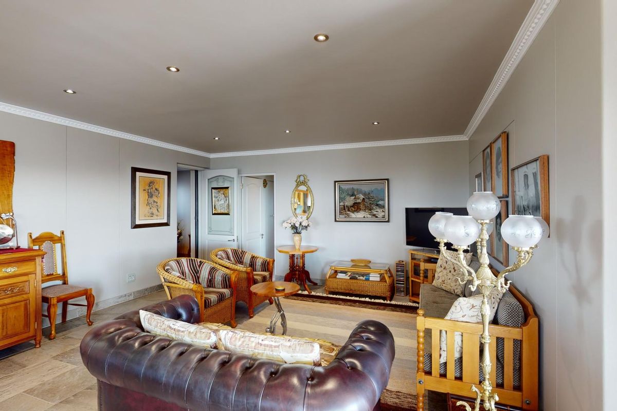 A spacious living room featuring neutral walls, crown molding, recessed downlights, and stone tile flooring, offering a comfortable and well-maintained living area.