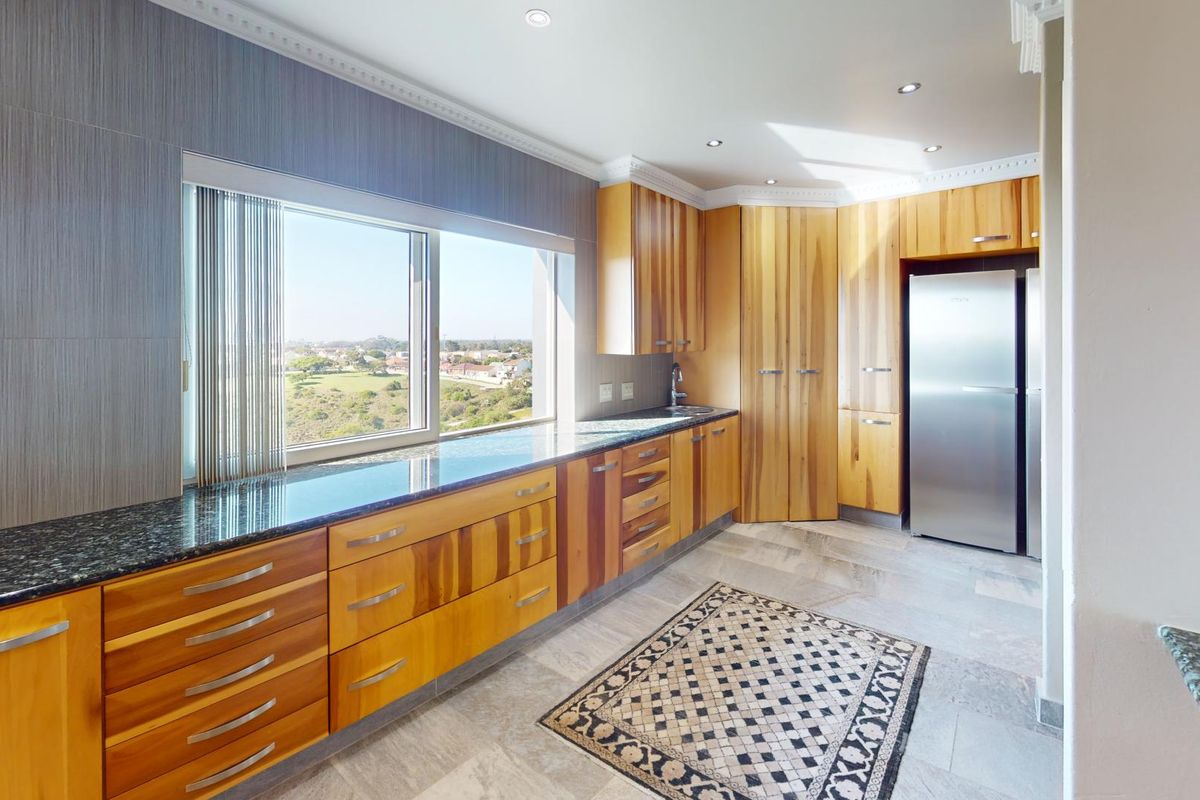 Modern kitchen featuring warm wooden cabinetry, granite countertops, and large windows offering scenic views, complemented by elegant tiled flooring and recessed lighting.