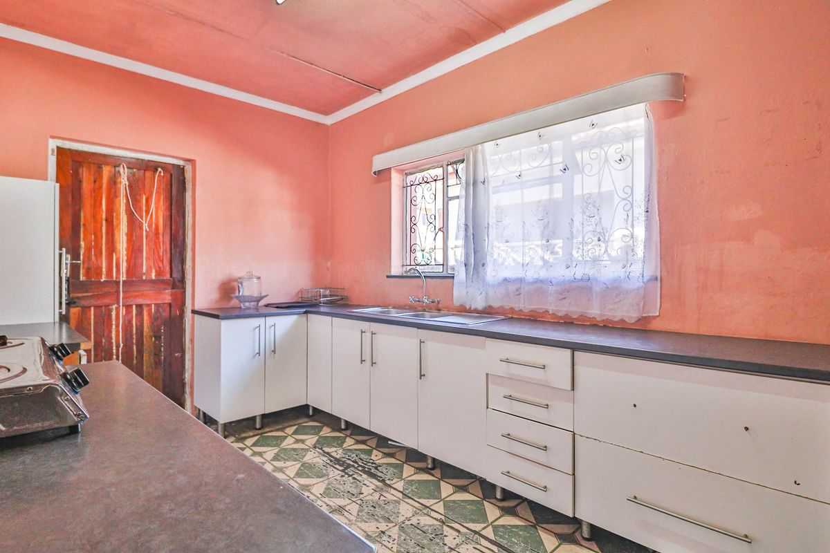 A dated kitchen featuring white cabinetry, a stainless steel sink, and patterned floor tiles, offering potential for a modern renovation.