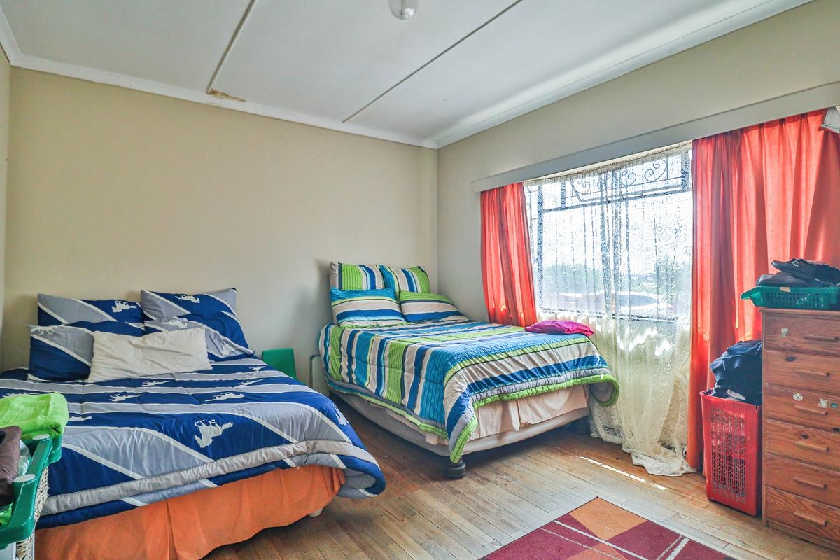 A bedroom featuring wooden flooring and a large window with curtains. The ceiling shows signs of water damage.