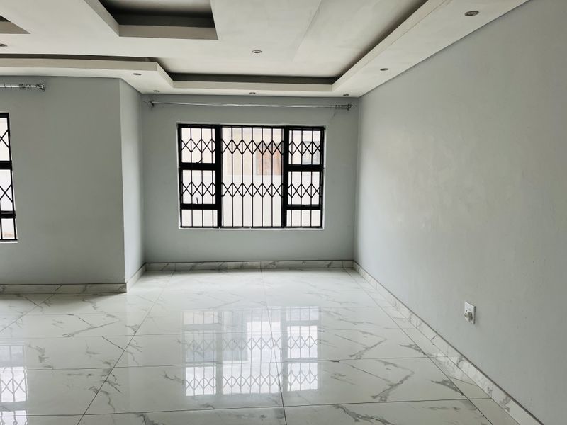A bright, empty living area featuring modern marble-look floor tiles, recessed ceiling detailing with downlights, and secure window burglar bars.