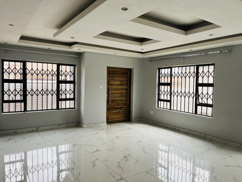 Spacious living area featuring polished marble-look floor tiles, a modern recessed ceiling with downlights, and secure window treatments.