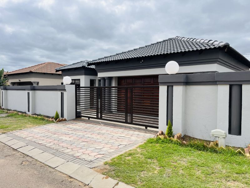 Modern front elevation featuring a secure perimeter wall, sliding gate, paved driveway, and a well-maintained tiled roof with integrated garage access.