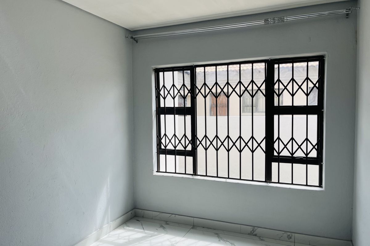 A bright, empty bedroom featuring modern tiled flooring and a window fitted with a black security gate.