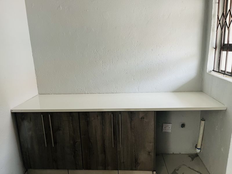 A functional laundry area featuring built-in cabinetry with a countertop, plumbing connections for appliances, and a security gate on the window.