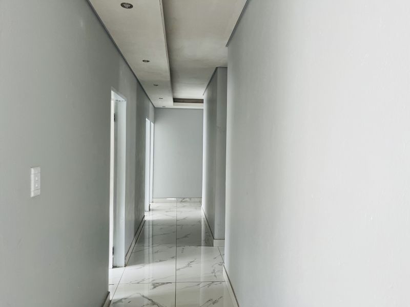 A bright, modern hallway featuring polished marble-look floor tiles and a contemporary dropped ceiling with recessed lighting.
