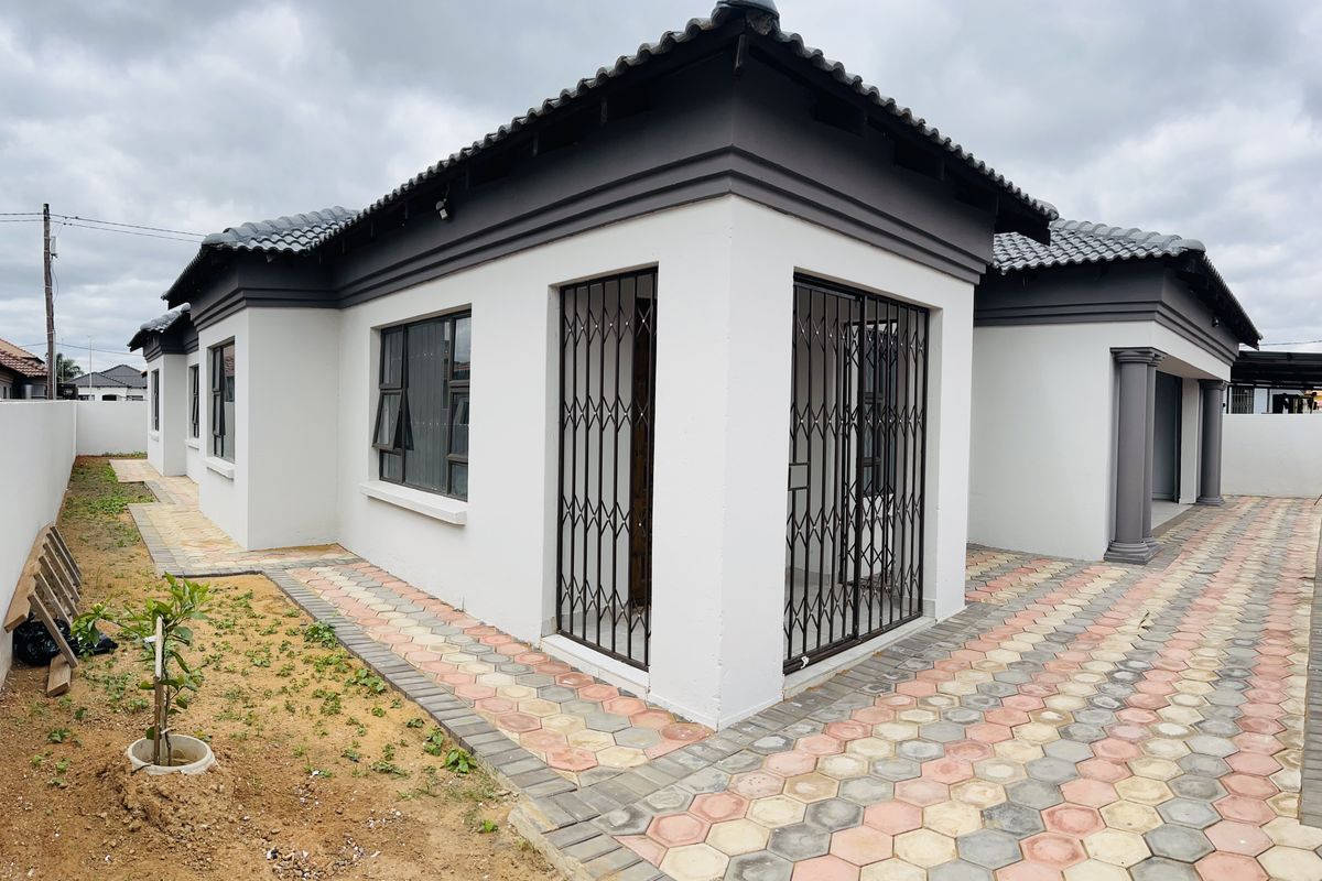 A well-maintained rear exterior view of the house featuring a tiled roof, paved pathways, and secure metal gates on the windows and doors.