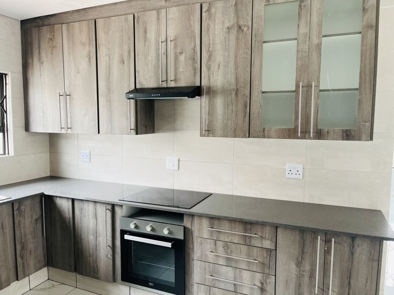 Modern kitchen featuring wood-grain cabinetry, stone countertops, integrated electric hob, oven, and extractor fan with a neutral tiled backsplash.