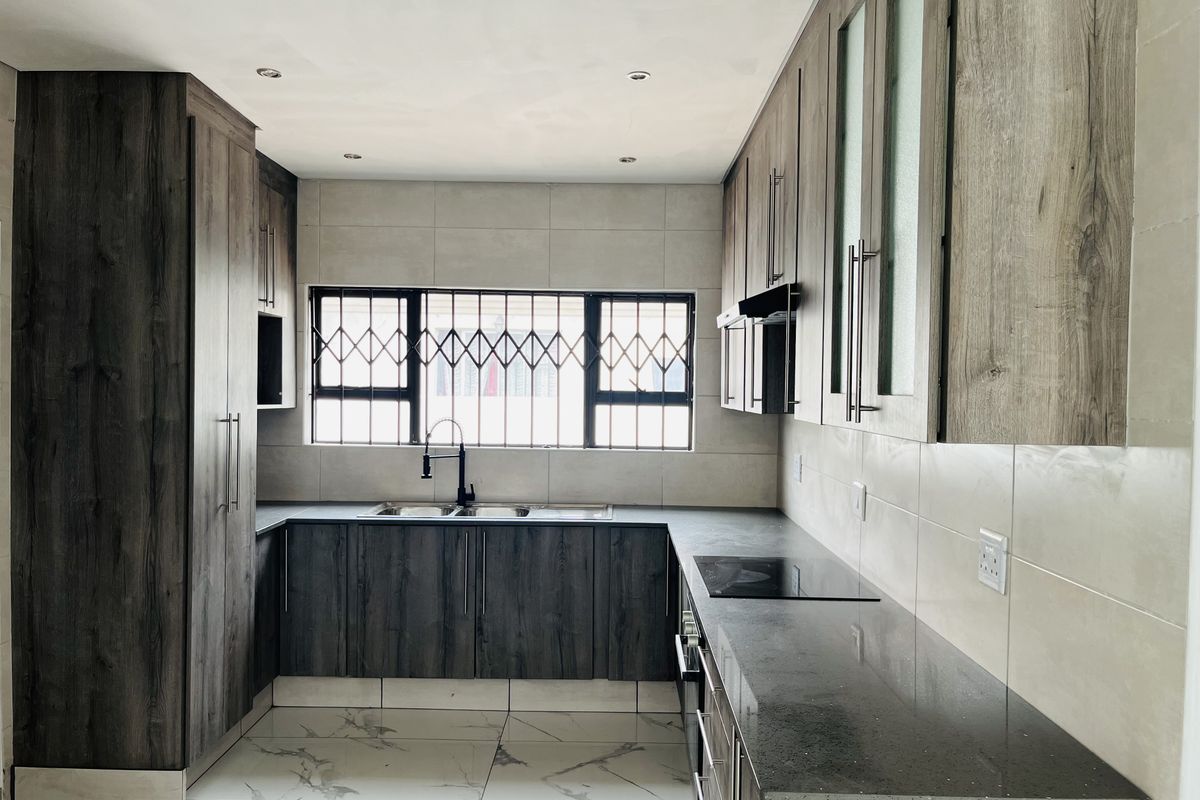 Modern kitchen featuring dark wood-grain cabinetry, stone countertops, integrated hob and oven, and large format marble-look floor tiles.