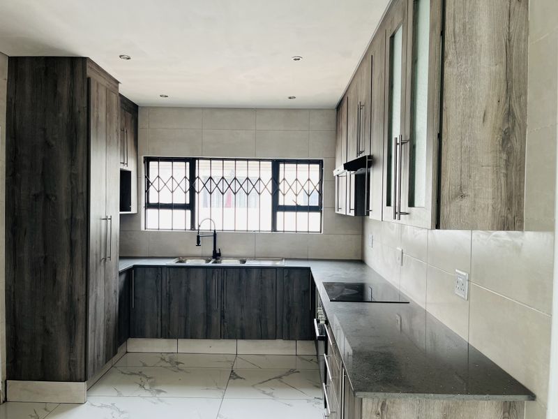 Modern kitchen featuring dark wood-grain cabinetry, stone countertops, integrated hob and oven, and large format marble-look floor tiles.