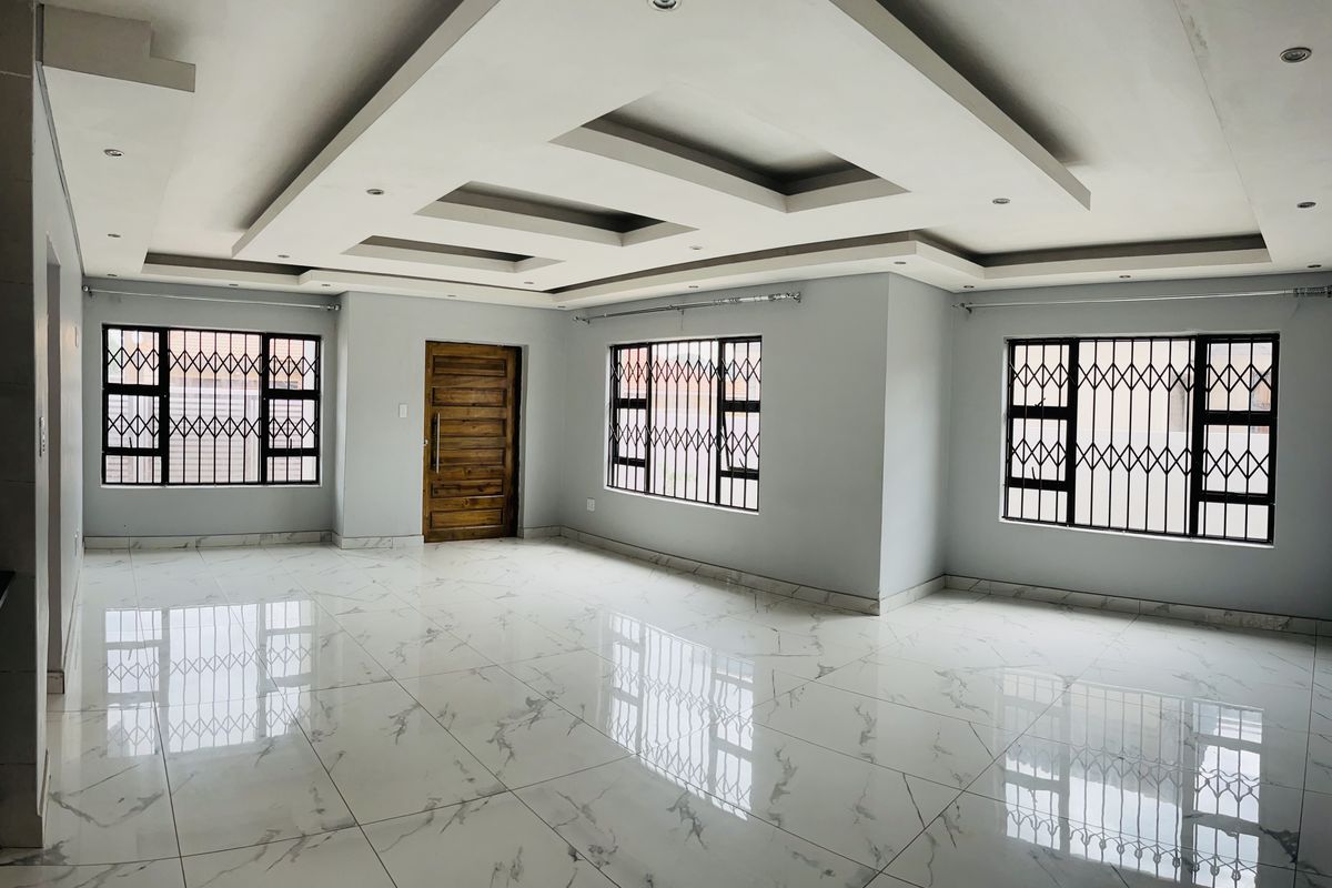 Spacious, open-plan living area featuring modern porcelain tile flooring, a decorative recessed ceiling with downlights, and secure window treatments.