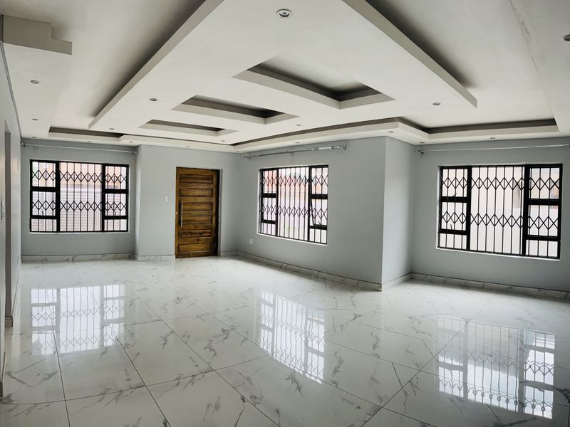 Spacious, open-plan living area featuring modern porcelain tile flooring, a decorative recessed ceiling with downlights, and secure window treatments.