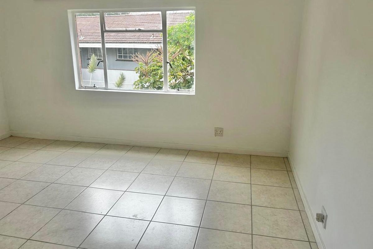 A bright, empty bedroom featuring neutral tiled flooring, a large window, and clean white walls, ready for personalization.