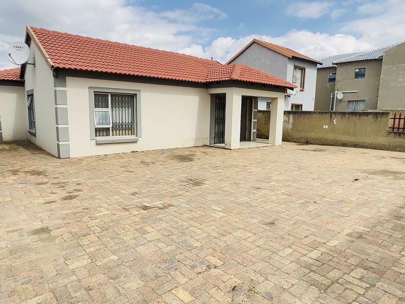 A detached house featuring a tiled roof, paved driveway, and secure entrance, set within a walled perimeter.
