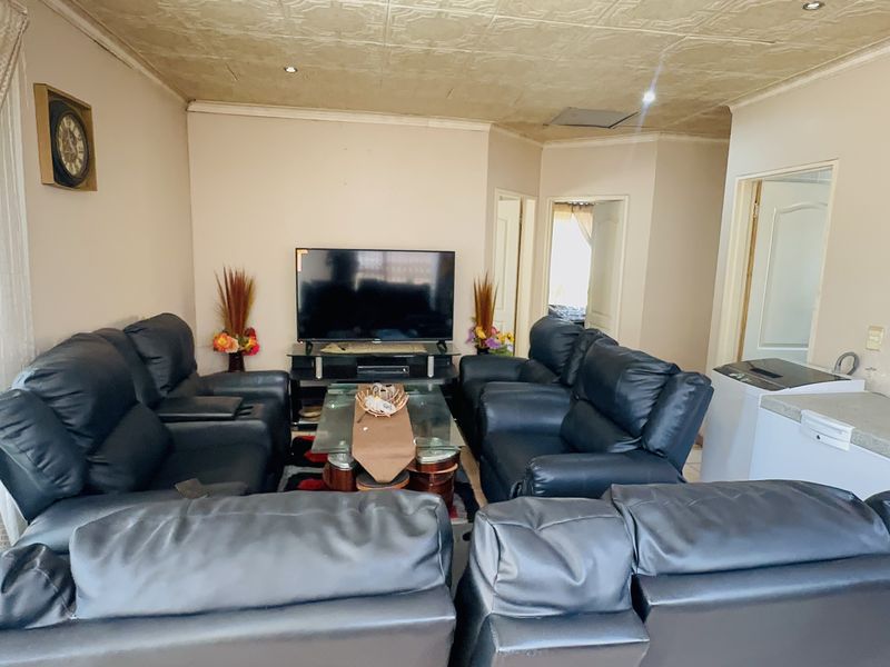 A living room featuring textured ceiling tiles, recessed lighting, and neutral wall finishes, providing a functional space for relaxation and entertainment.