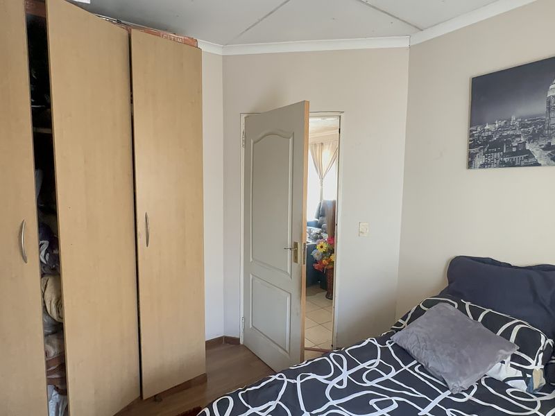 A bedroom featuring laminate flooring and a built-in wardrobe, with a doorway leading to an adjacent living space.