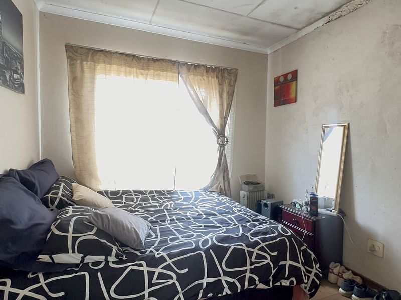 A bedroom featuring a window and coved ceiling, currently showing significant signs of wear including peeling paint and water damage on the ceiling.