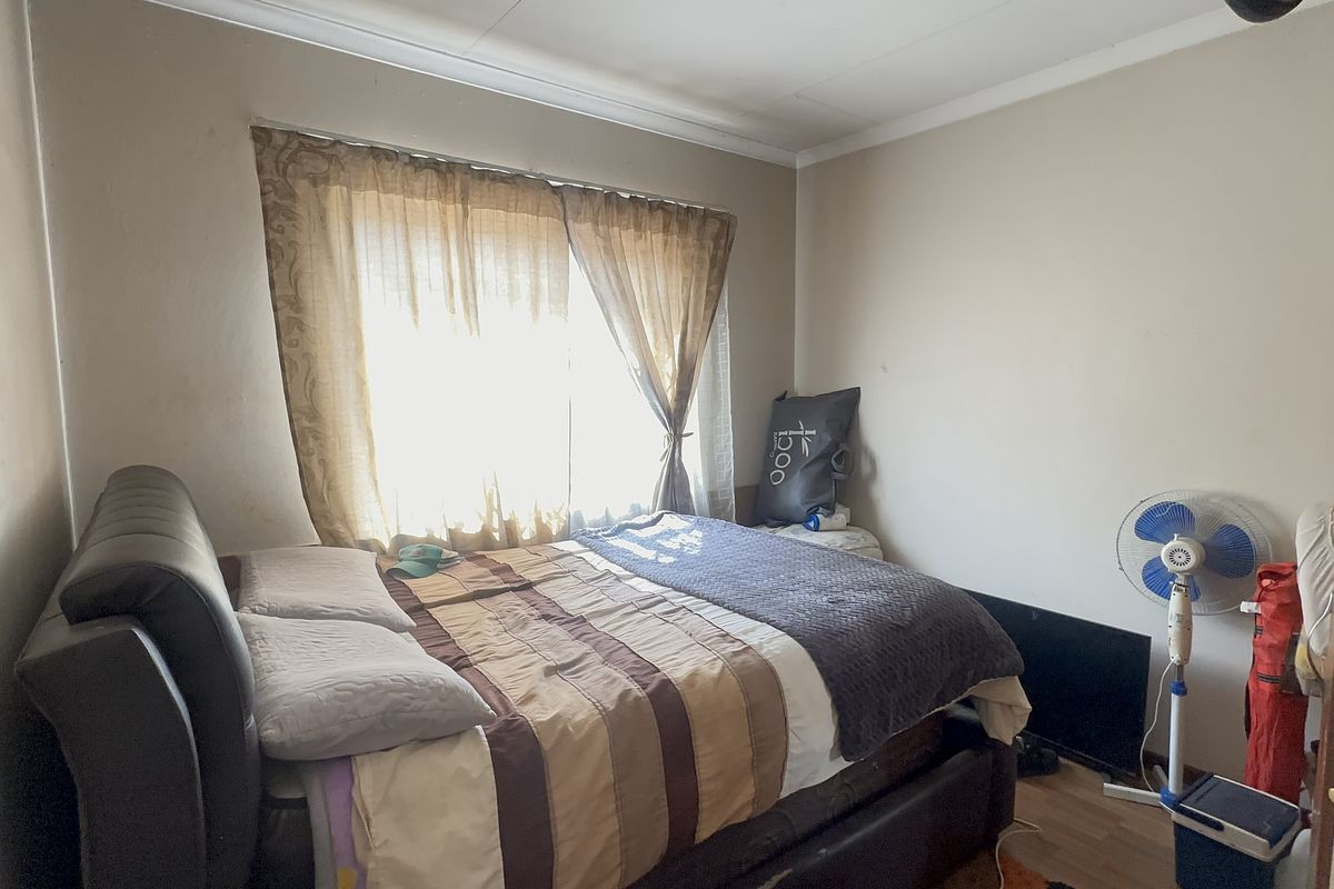 A standard bedroom featuring laminate flooring and a window with curtains, requiring cosmetic updates to improve the overall condition of the wall finishes.