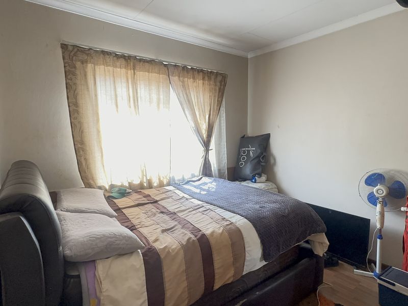 A standard bedroom featuring laminate flooring and a window with curtains, requiring cosmetic updates to improve the overall condition of the wall finishes.