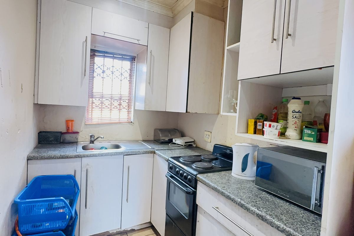 A compact kitchen featuring white cabinetry, laminate countertops, and a built-in electric stove, offering a functional layout in need of cosmetic updates.