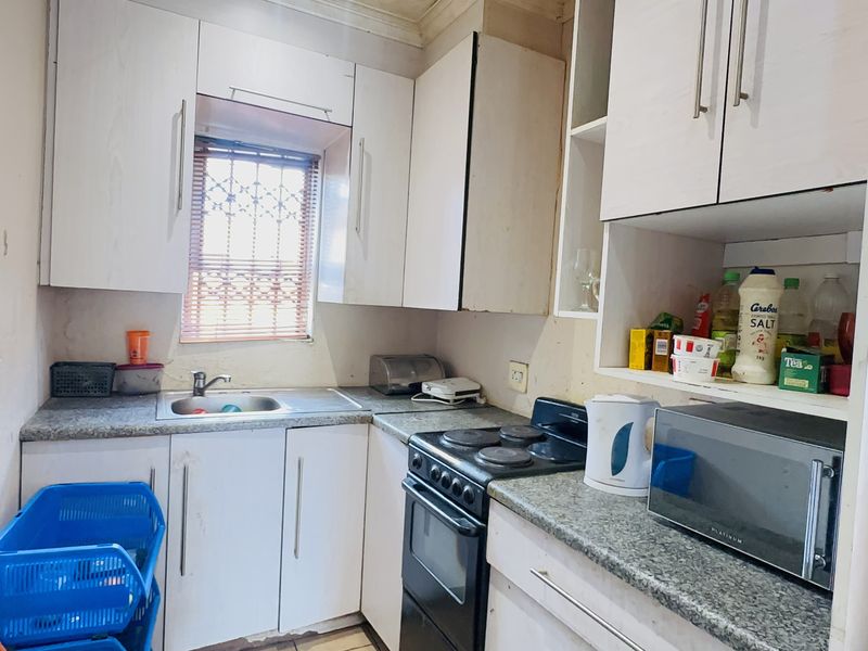 A compact kitchen featuring white cabinetry, laminate countertops, and a built-in electric stove, offering a functional layout in need of cosmetic updates.