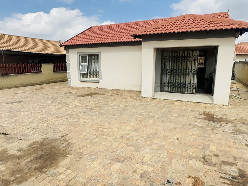 Rear exterior view of the house featuring a large paved courtyard, perimeter walling, and a covered patio area with security gates.