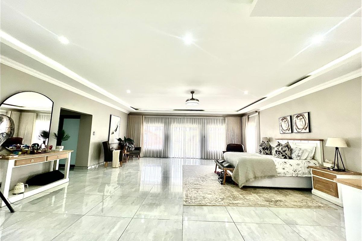 Spacious primary bedroom featuring large format floor tiles, recessed ceiling lighting, and expansive glass sliding doors leading to an outdoor area.