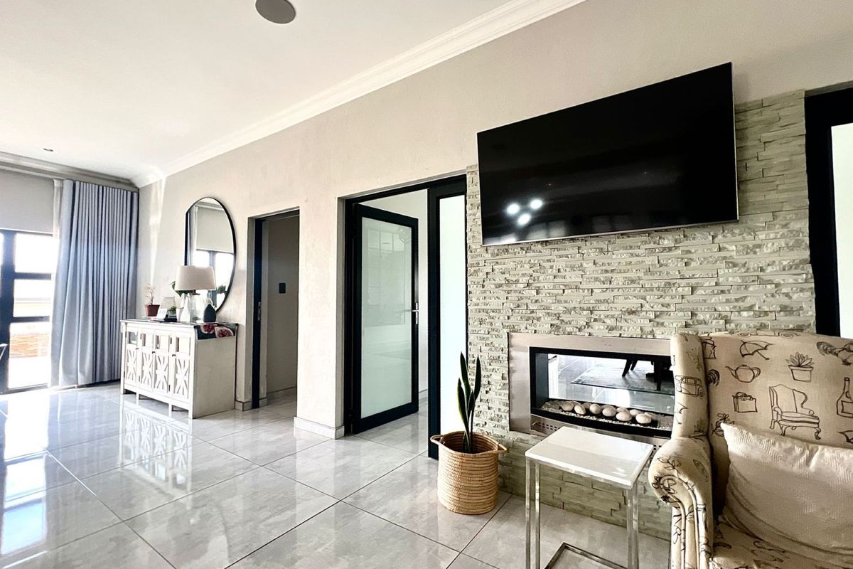 Spacious living room featuring large format floor tiles, a modern stone-clad fireplace, and sleek black-framed glass doors leading to adjacent rooms.