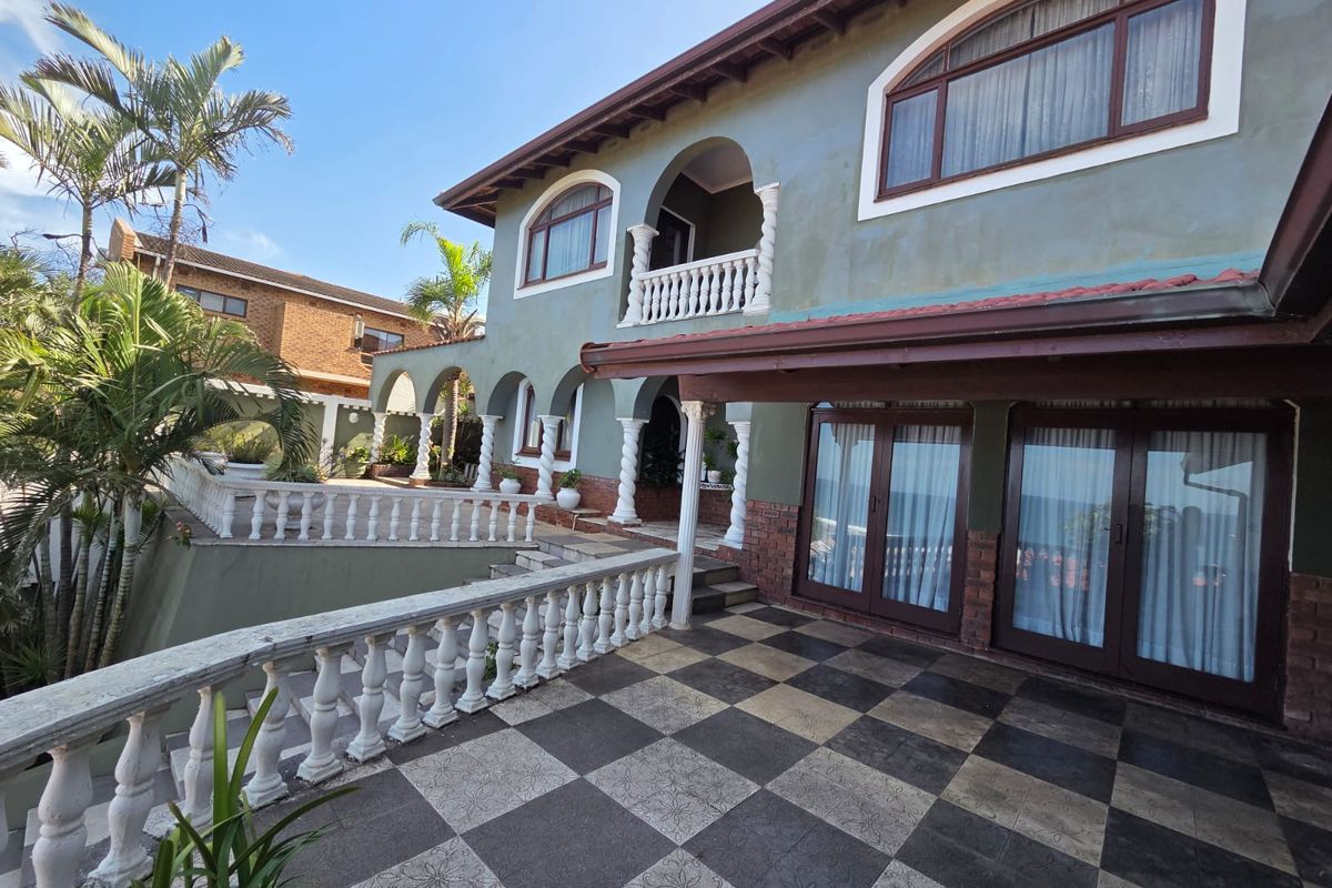 Rear exterior view of a multi-story house featuring a large tiled patio, decorative balustrades, arched architectural details, and sliding glass doors.